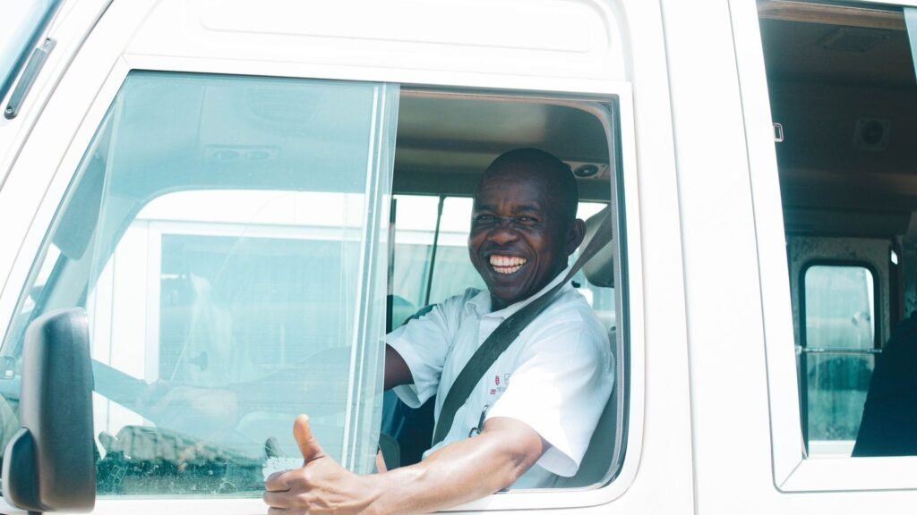 Airport Driver Jobs UAE 2026: Salary, Requirements & Hiring Guide Smiling driver in uniform seated at the wheel of a white passenger van