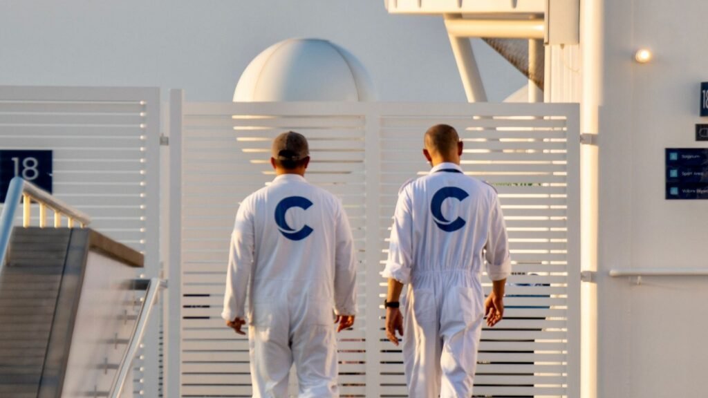 Cruise Ship Jobs in Dubai 2026 Two cruise ship crew members in white uniforms walking along an upper deck of a cruise ship