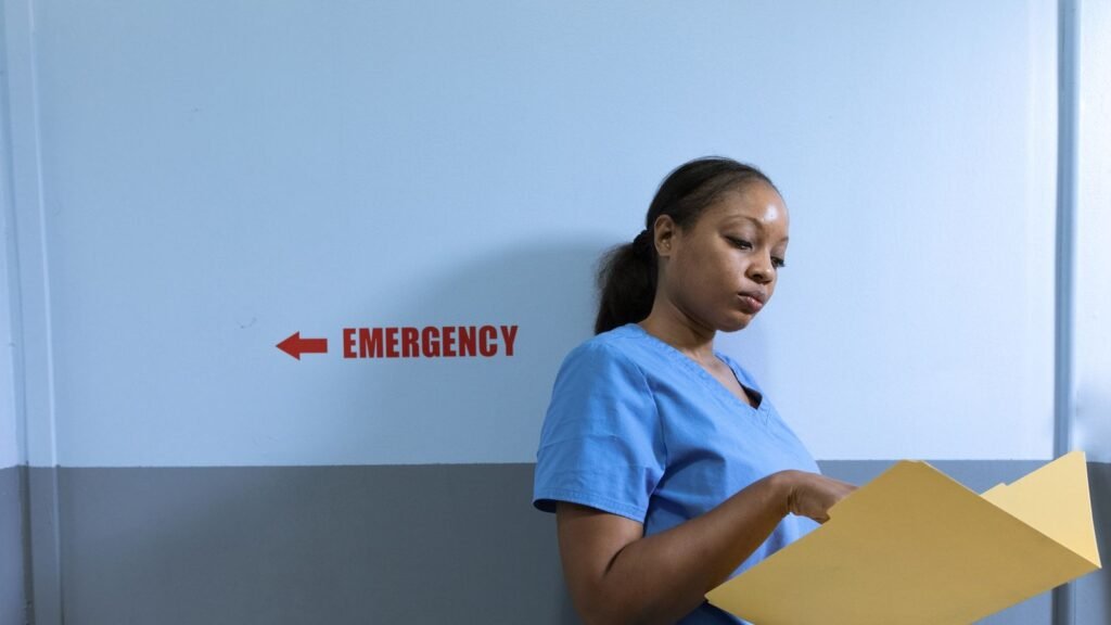 Hospital Jobs UAE 2026 – Requirements, Salary & Hiring Guide Nurse in blue scrubs reading a patient file beside an emergency department sign