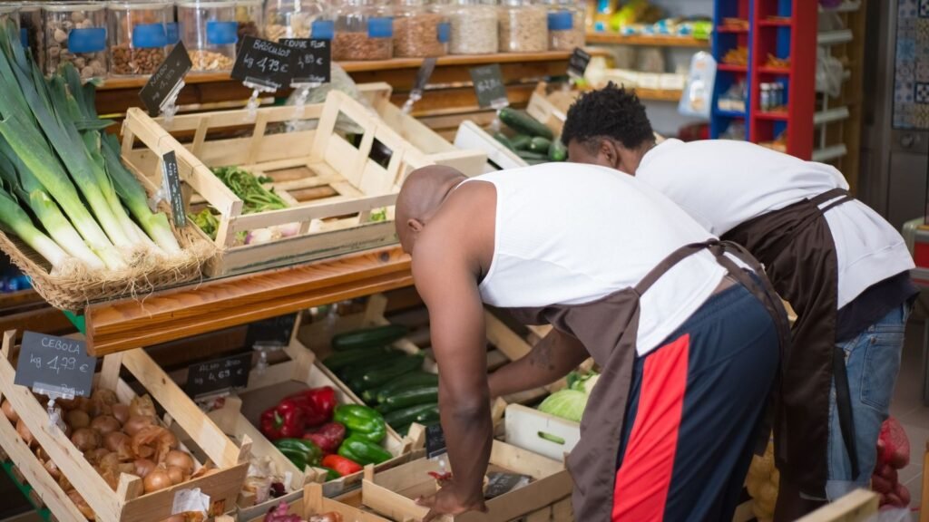 Supermarket Jobs in Dubai 2026 Two supermarket staff members in aprons arranging fresh vegetables in the produce section of a grocery store
